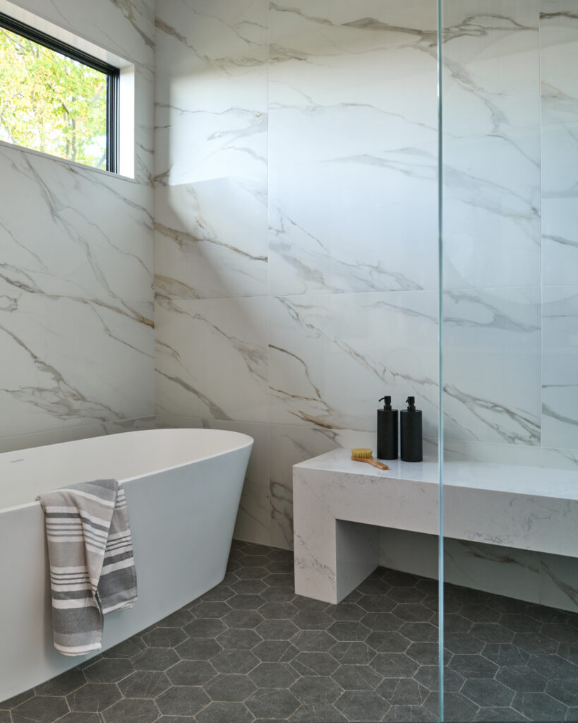 Primary bathroom with walk-in shower, large soaker tub, custom stone bench and dark grey hexagon tile flooring, part of a custom home designed by a Toronto-area interior design firm Erin Interiors.