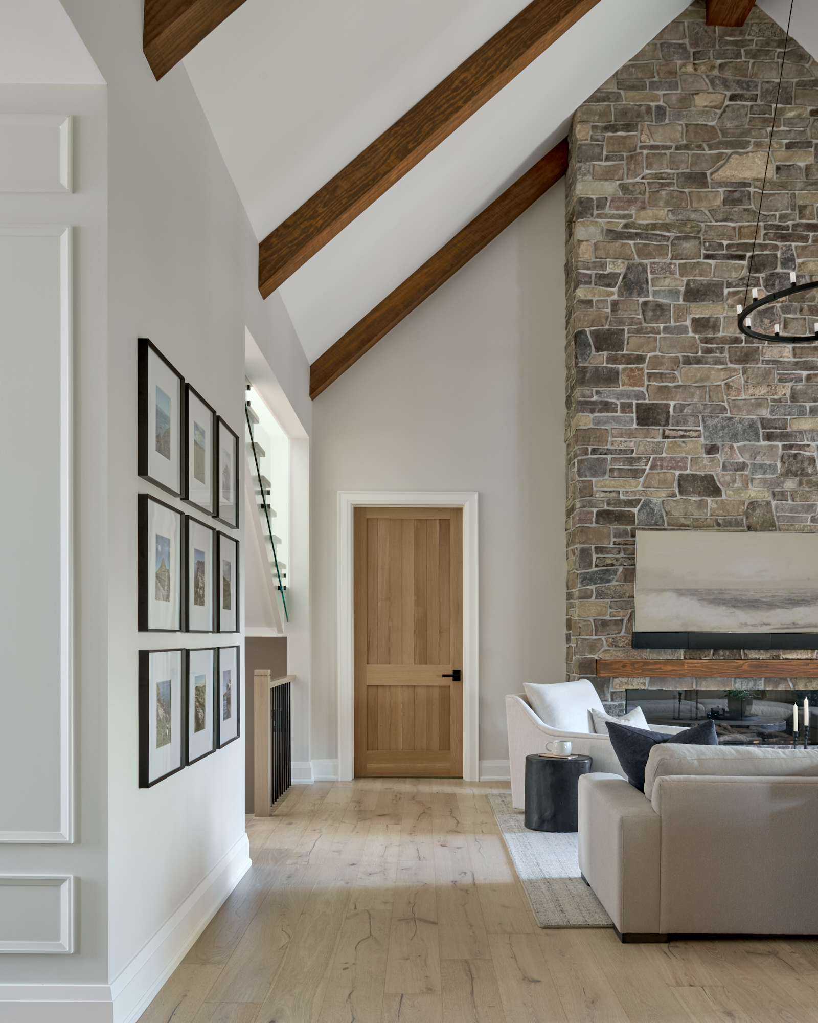 Custom home living room featuring pale oak flooring, a floor-to-ceiling stone fireplace, white accent chair and chic neutral sofa, designed by a Toronto-area interior design studio.