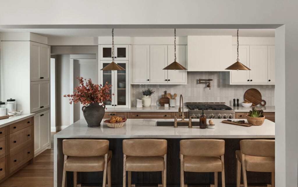 Modern kitchen design with brass pendant lights above large kitchen island with counter height bar stools with neutral leather backs and white kitchen cabinets in Simply White by Benjamin Moore