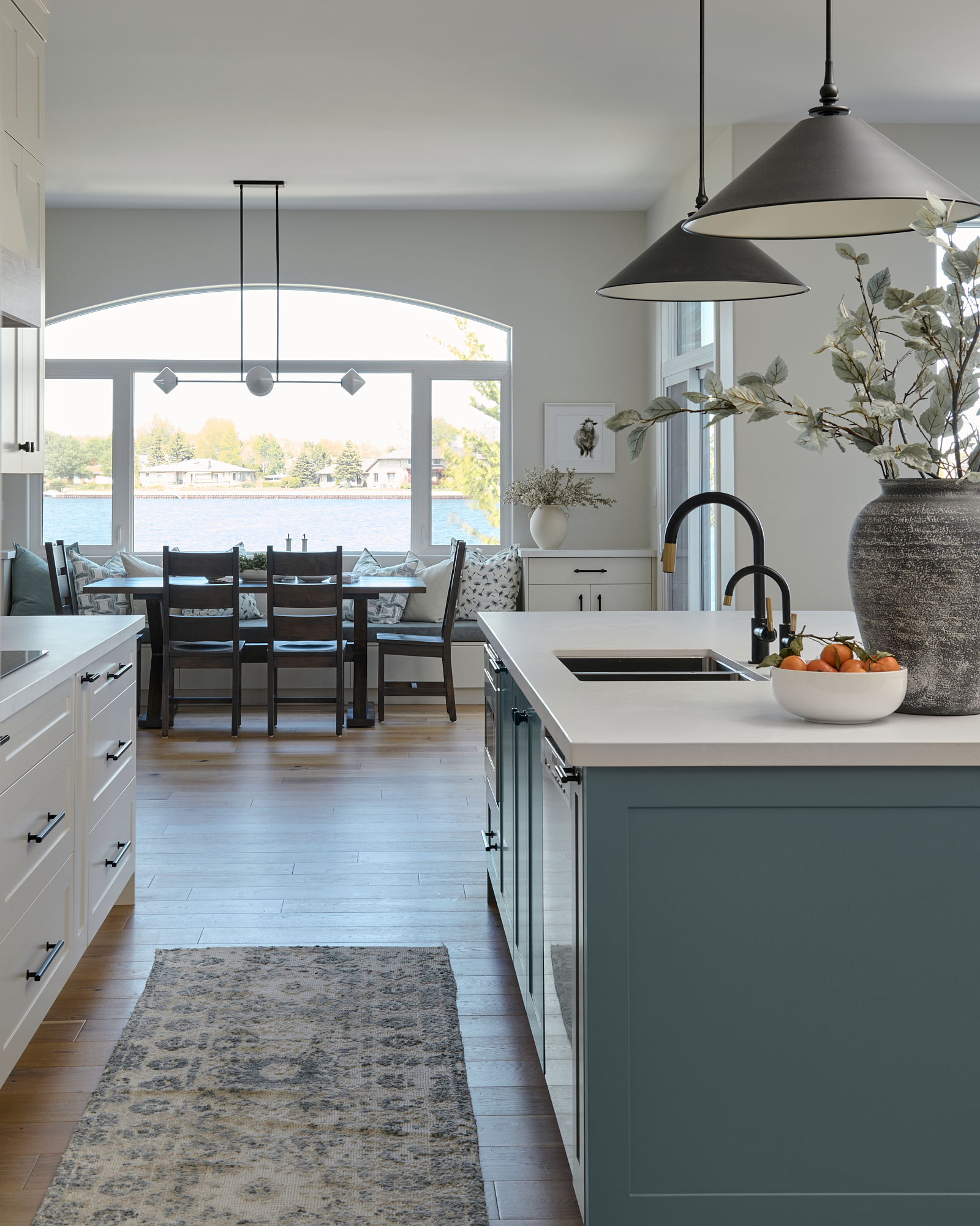 A modern kitchen renovation by Erin Interiors, an interior design team in Whiby, Ontario, features lower cabinetry in Duxbury Gray by Benjamin Moore and upper cabinetry in Edgecomb Grey by Benjamin Moore. The kitchen island has a built in sink and there is a runner in the kitchen between the island and kitchen counter.
